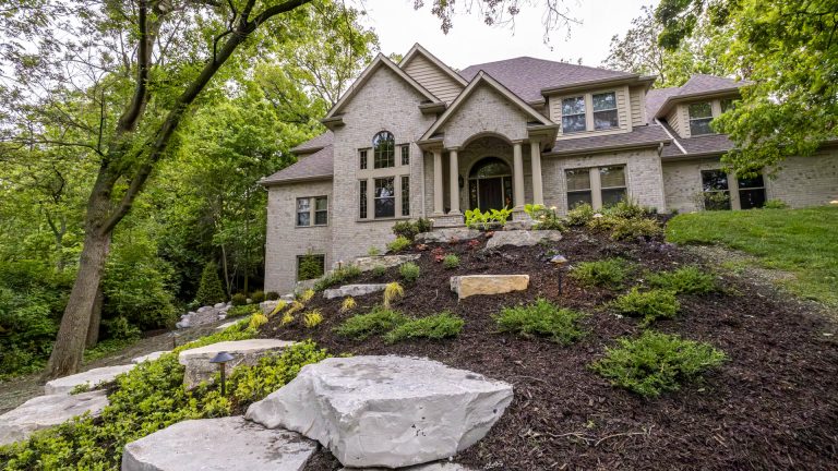 Landscaping design with stone steps leading to a large home. Mulch and plants.
