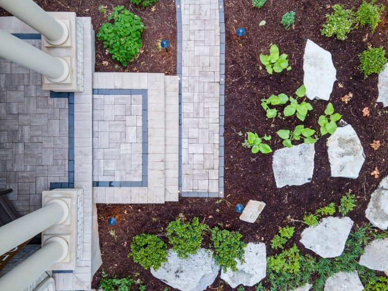 Aerial view of landscape design with stone pathway, plants, and patio with columns. Hardscape and softscape elements.