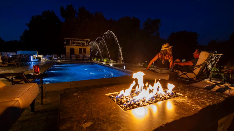 Night landscaping with a pool, fire pit, and water fountains. Outdoor living.