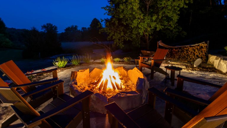 Night landscape with stone fire pit and Adirondack chairs. Outdoor living space.