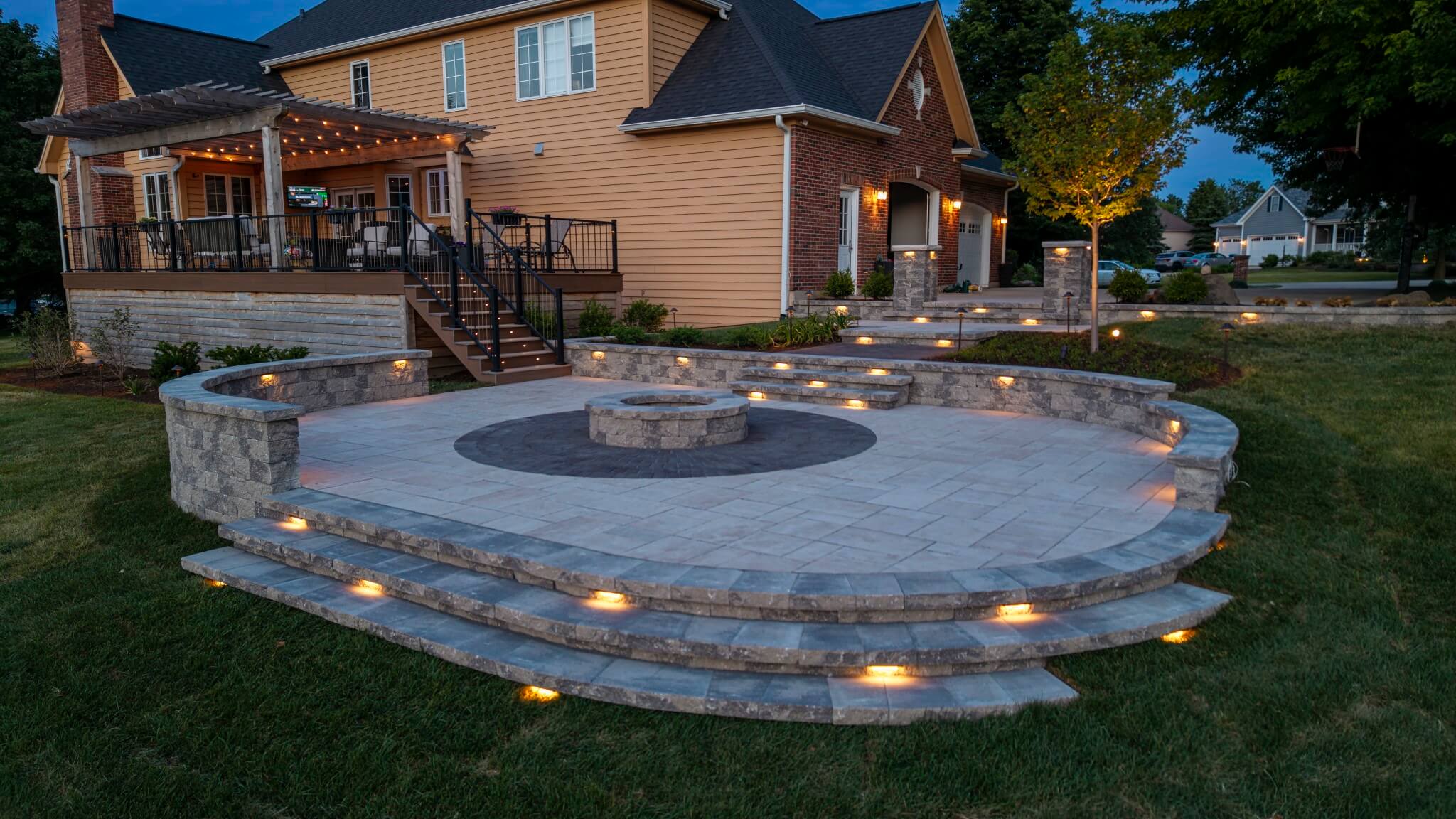 Overhead view of a semi-circular paver patio at twilight with glowing low-voltage lights embedded in the stone steps.