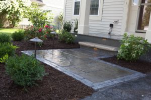 Stone walkway leads to home's porch. Landscape lighting and mulch add to the curb appeal. Garden with flowers.