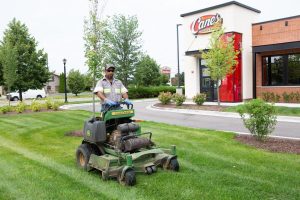 Commercial lawn mowing. Worker on John Deere mower cuts grass at Raising Cane's. Landscape maintenance.