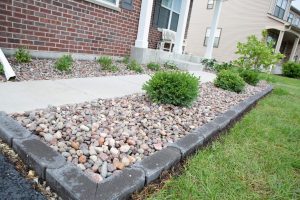 Landscaping with red flint stone and concrete edging. Bushes and green grass. Home exterior.