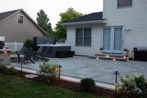 Residential patio installation with Unilock Beacon Hill pavers, hot tub, chairs, and landscape lighting.