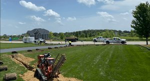 Drainage service installation. Trenching machine digging a trench for yard drainage. Sod replacement. Trucks and workers.