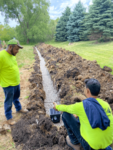 Drainage service installation. Workers installing a French drain system with gravel and drain box in a yard.