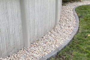 Above-ground pool with rock landscaping. White rocks and a gray brick border. Green grass.