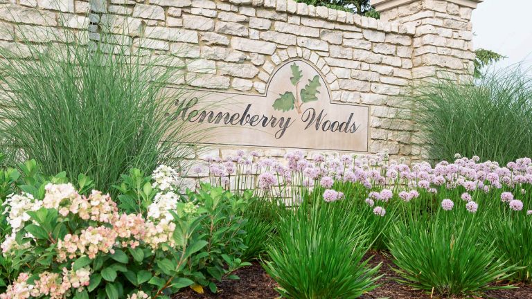 Henneberry Woods entrance sign with commercial landscaping. Stone wall, flowers, and ornamental grasses.