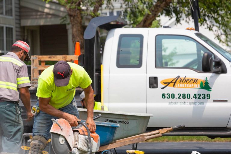 Photo of a worker in front of an Arbeen truck cutting landscape stone tiles with a large saw
