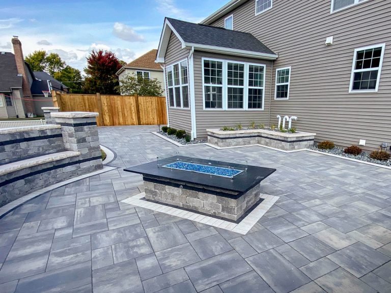 Residential brick paver patio with firepit installation. Commercial landscaping with stone seat wall.