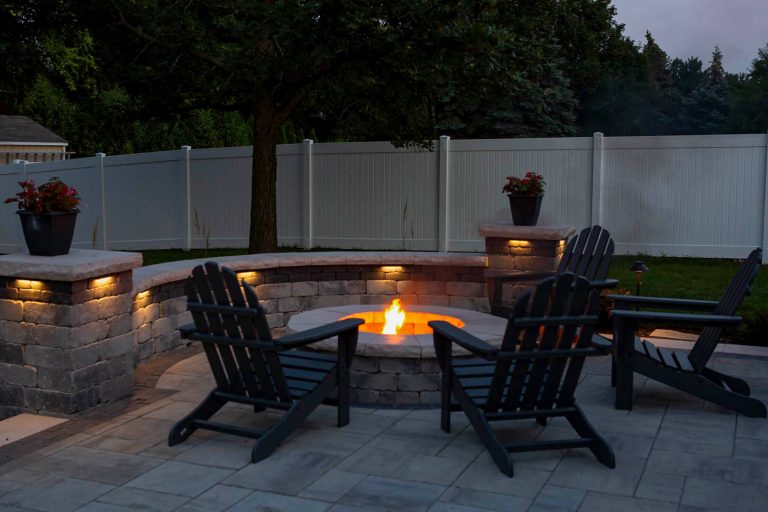 Residential brick paver patio with firepit installation at night. Landscape design with outdoor seating.