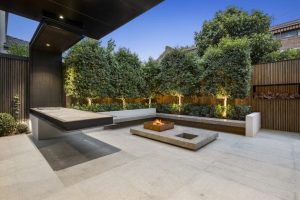 Modern backyard design with fire pit, outdoor kitchen, and lush landscaping. Stylish outdoor living space.