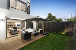 Modern backyard patio with outdoor furniture, umbrella, wood deck, and green grass. Contemporary home design.