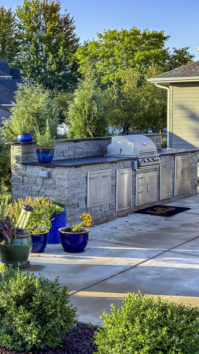 Home 47 Custom outdoor kitchen with grill and landscaping. Stone kitchen island with stainless steel appliances.