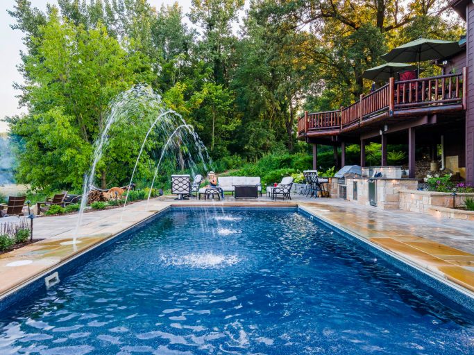 Custom pool with water feature and landscape lighting. Outdoor kitchen and patio with seating. Berst-Millington-Arbeen Landscaping.