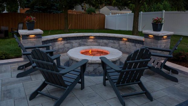 Residential brick paver patio with firepit installation. Commercial landscaping with outdoor chairs at night.