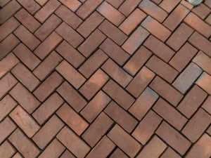 Red brick pavers laid in a classic herringbone pattern for a patio surface.