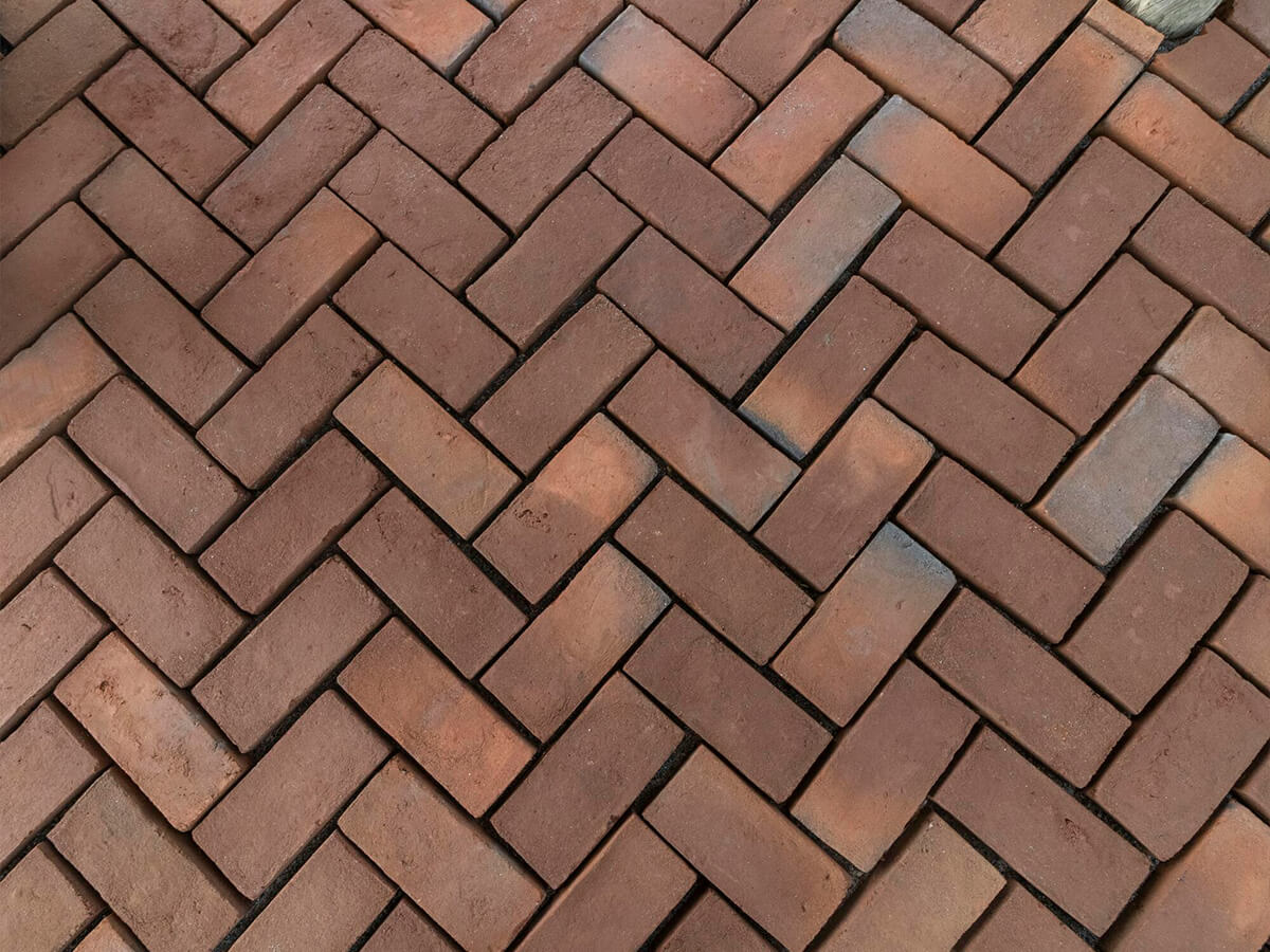 Red brick pavers laid in a classic herringbone pattern for a patio surface.