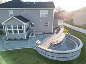 Custom patio design with fire pit. Outdoor living space with seat wall and paver patio. Backyard landscaping.